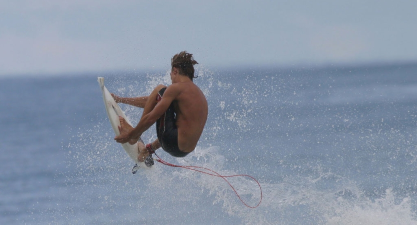 A person catches air while surfing on blue water. 